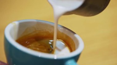 Cafe latte sanatından yapılmış barista. Kahve bardağındaki kalp şeklinde. Sütü yavaşça mavi bir fincana dökerek latte yapmak. Yakın plan..