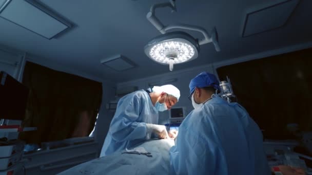 医生在手术室做手术 医院黑暗房间里穿着医疗制服在明亮灯下做手术的专业外科医生 — 图库视频影像
