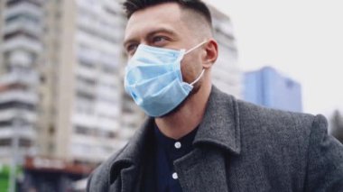 Erkek turist, yüzü virüslerden koruyor. Tıbbi maske takan yakışıklı bir adam şehirde yürürken koronavirüsü engeller. Yavaş çekim.