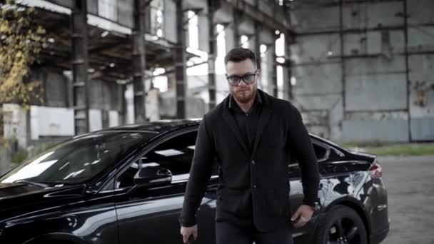 强壮的男人在废弃的地方拿着球棒古旧的空荡荡的工厂里 戴着眼镜 身穿黑色衣服 穿着昂贵的汽车底座向前走着 — 图库视频影像