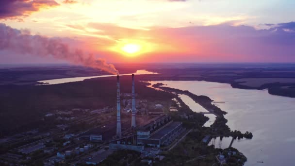 日没時のカラフルな空の背景にある工場 夜の産業パイプから空気を満たす有害な煙 川の近くで製造しています エアリアルビュー — ストック動画