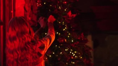 Kadın yılbaşı ağacını süslüyor. Genç bir kadının arkası, kış tatilinden önce Noel oyuncakları asar. Adam karısına gelir. Kırmızı ışık videosu.