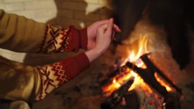 Şöminenin yanındaki kadın ve erkeğin elleri. Birbirlerine aşık çiftler şöminenin yanında ellerini ısıtıyorlar. Evde romantik bir ortam var..