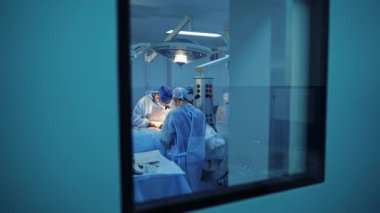 Modern tıp merkezinde cerrahi işlem. Ameliyathanede. Küçük pencereden ameliyathaneye doğru bak. Hareket kamerası geri.