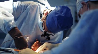 Profesyonel doktor bir hastaya ameliyat yapar. Tıbbi şapkalı ve fenerli cerrah, asistanıyla birlikte cerrahi aletlerle ameliyat yapıyor. Yakın plan..
