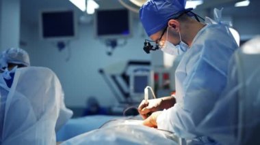 Klinikte ameliyat. Tıbbi maskeli profesyonel bir cerrah ve kafasında el feneri olan bir hasta üzerinde ameliyat yapıyor. Erkek asistan ameliyathanede doktora yardım ediyor..
