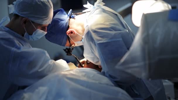 手術中の医師 医療ランプの下で専門外科医による操作プロセス 手術を行う医療専門家および男性アシスタント — ストック動画