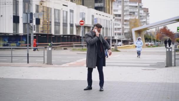 코트를 잘생긴 남자는 야외에서 사업가 전화와 거리에 시계를 슬로우 — 비디오