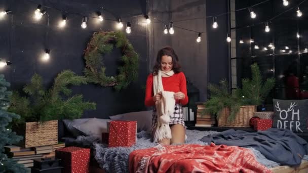 クリスマスに幸せなモデルの肖像画 ニットキャップを着てカメラにポーズする笑顔の若い女性 クリスマスの装飾された背景のベッドに美しい女の子 — ストック動画