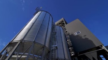 Gümüş kaplar dışarıda. Mavi gökyüzüne karşı modern tarım kompleksi. Büyük tahıl asansörleri. Endüstriyel fabrika Aşağıdan görüntüle.