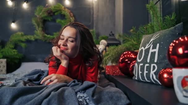クリスマスの装飾の背景にハッピーな女性 赤いセーターの若い女性は冬の休日に喜んでベッドの上に横たわっています ハッピーウィンターホリデーコンセプト — ストック動画