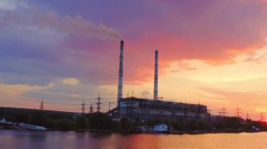Gün batımında sanayi bölgesinde. Nehrin kıyısındaki güzel pembe gökyüzündeki fabrika. Akşamları endüstriyel pipodan zararlı dumanlar çıkıyor..