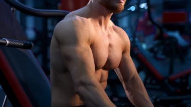 Spor merkezinde dinlen. Antrenman sırasında gömleksiz bir adam mola veriyor. Atletik adam elinde bir şişe suyla simülatörde oturuyor. Yakın plan..