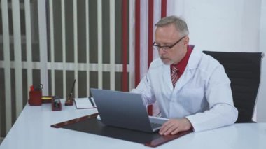 Yaşlı doktor laptopta video görüşmesi yapıyor. Üst düzey erkek doktor web sohbetinde web kamerasıyla iletişim kuran bilgisayar ekranına bakarken hastayla konuşuyor. Teletıp kavramı.
