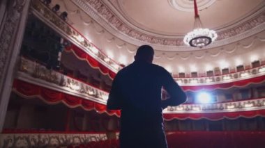Tiyatro salonunun önündeki aktör. Adam sahnede duruyor ve gösteriden önce jestlerle konuşuyor..