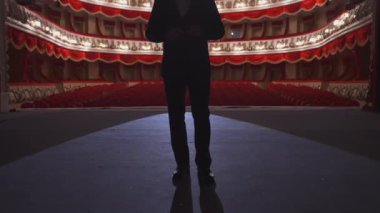 Takım elbiseli bir adam konser salonuna geri dönüyor. Kırmızı ve beyaz renklerde klasik tiyatro salonunun arka planında tanınmayan aktörün karanlık silueti..