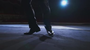 Aktör bacakları sahnede dans ediyor. Siyah ayakkabılı bir adam karanlık ışıkta tiyatro salonunda dans ediyor. Yakın plan..
