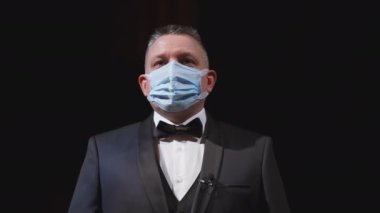 Zarif takım elbiseli ve tıbbi maskeli bir adam. Tiyatronun sahnesinde duran koruyucu maskeli bir aktörün portresi. Adam maskeyi yüzünden çıkarıyor. Koronavirüs salgını.