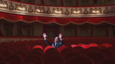 Büyük salonda takım elbiseli başarılı bir adam tek başına. Aktör adam boş kırmızı koltukların arasında oturuyor ve opera salonunda şarkı söylüyor..