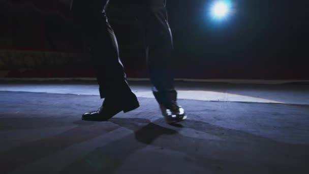 俳優の足がステージで踊っている 暗い光で劇場ホールに向かって踊る黒い靴の男 クローズアップ — ストック動画