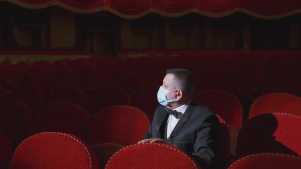 空の劇場で医療マスクをした悲しい男 金持ちは空っぽの赤いアームチェアの間に一人で座り オペラホールで眠っている ロックダウンコンセプト — ストック動画