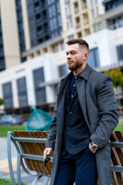 Parkta bir bankın yanında duran bir adam. Parktaki Huzurlu Bir An: Doğanın Güzelliğini Düşünen Bir Adam, Yeşillik ve Huzur Çevresinde