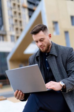 Dizüstü bilgisayar kullanarak çıkıntıda oturan bir adam. Odaklanan Adam: Kente Bakış Amaçlı Bir Çıkıntı Üzerinde Dengeleme Çalışması ve Serenity