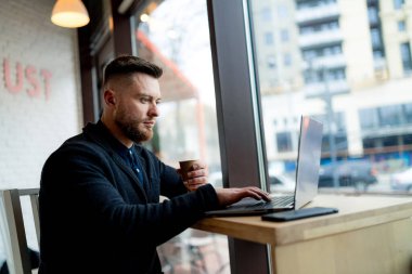 Dizüstü bilgisayar kullanarak masada oturan bir adam. Ofiste Üretken bir gün: Dizüstü bilgisayarıyla uğraşan bir adam