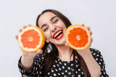 Suratının önünde iki parça greyfurt tutan bir kadın. Citrus Maskesi: Bir Kadının Greyfurt Dilimleriyle Eğlenceli Karşılaşması