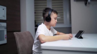 Tabletli şirin bir çocuk. Çocuk tablete bakıyor ve mutfakta yemek yiyor.