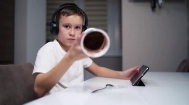 Çocuk yemek yiyor ve tablet seyrediyor. Çocuk tatlı yiyor ve tablet ekranına bakıyor.