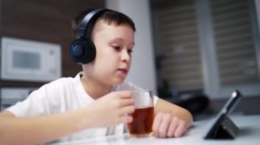 Çocuk tablete bakıyor. Tablette çizgi film izlerken kahvaltıda çay içen tatlı çocuk.