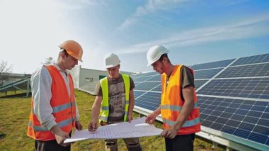 Güneş enerjisi santralinin mühendisleri. Fotovoltaik panellerin arka planında projeli erkek işçi güneş enerjisi santrali
