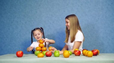 Meyveli mutlu küçük kız. Küçük kız masada meyvelerle oynuyor.