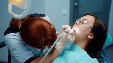 Hasta dişçi koltuğunda oturuyor. Üniformalı diş hekimi hastaya diş ameliyatı yapıyor.