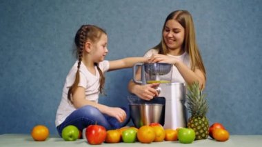 Küçük kız taze meyve suyu yapıyor. Mutlu bir anne ve kızı masada oturmuş, taze meyve suyu hazırlıyorlar.
