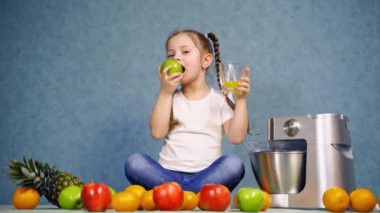 Elinde bir bardak portakal suyu olan kız. Küçük kız ev yapımı meyve suyu ile elma yiyor.