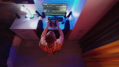 İnsan sürücü simülatörünün en üst görüntüsü. Bilgisayarlı genç adam evde araba yarışı video oyunu oynuyor.