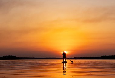 Gün batımında suda sörf tahtasının üzerinde duran biri.