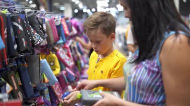 Çocuklu bir kadın dükkânda. Kırtasiyede ailesi olan küçük çocuk okul malzemelerini seçiyor.