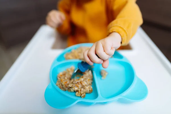 A child is eating cereal out of a blue bowl. A Hungry Baby Enjoying Cereal from a Blue Bowl, While Wearing a Feeding Bag
