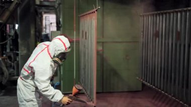 Metal parçalarının toz tabakası. Koruyucu giysili işçiler metal ürünlerine barut boyası sıkarlar.