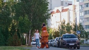 Kaldırımda yürüyen T-Rex. Şehirde dinazor kostümü giyen biri var.