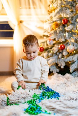 Neşeli bir çocuk Noel Ağacı 'nın önünde oyuncakla oynuyor. Küçük bir çocuk Noel ağacının önünde oyuncakla oynuyor.