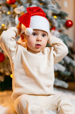 Neşeli küçük bir çocuk, güzel Noel Ağacı 'na hayranlık duyuyor. Küçük bir çocuk Noel ağacının önünde oturuyor.