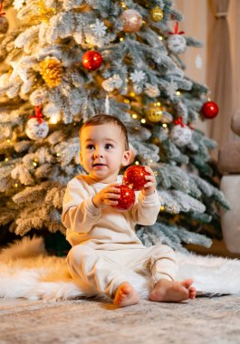 Bir Noel ağacının ışıldayan ışıklarıyla büyülenmiş neşeli bir bebek. Noel ağacının önünde oturan bir bebek