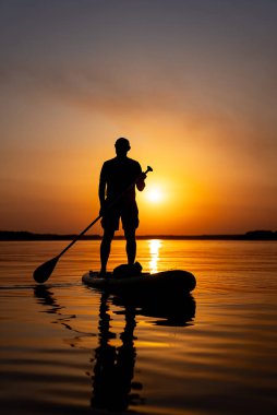 Kristal berrak sularda sakin bir sabahın tadını çıkaran adam. Suda kürek tahtasında duran bir adam.