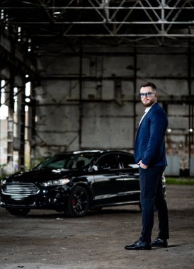 Siyah bir arabanın yanında duran takım elbiseli bir adam. Siyah bir arabanın yanında duran takım elbiseli bir adam.