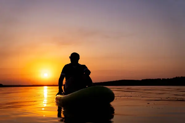 A Serene Moment: A Man Contemplating Life on a Raft as the Sun Sets. A man sitting on a raft in the water at sunset