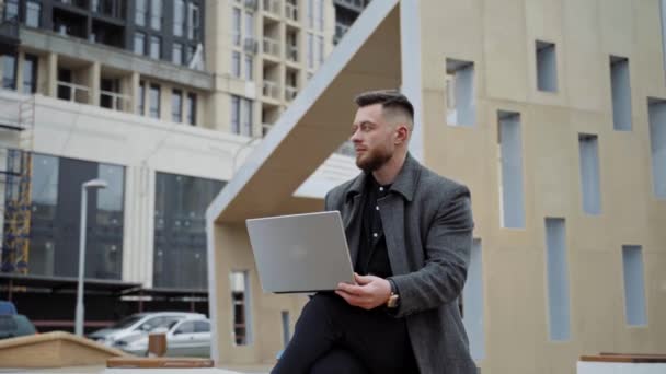 男性在室外使用笔记本电脑 年轻英俊的自由职业者坐在街上用新的现代笔记本电脑 — 图库视频影像